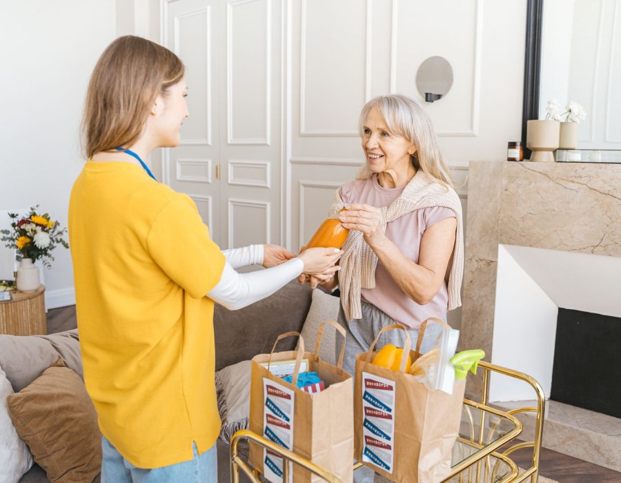 Pflegekraft überreicht einer Seniorin Einkäufe zu Hause
